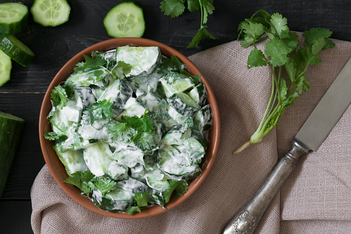 Cucumber salad with coriander and yogurt dressing on the black wooden background