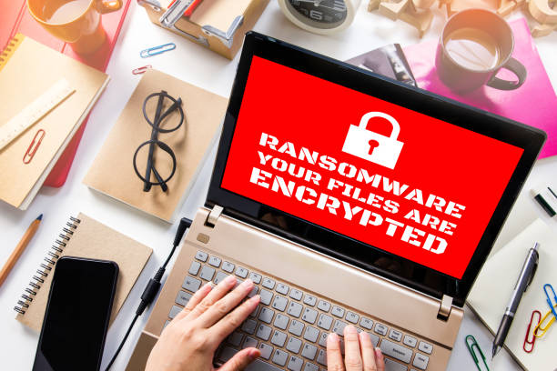 laptop sulla scrivania mostrando schermo rosso con icona lucchetto.computer è stato bloccato l'accesso ai dati con ransomware - spam computer hacker computer keyboard e mail foto e immagini stock