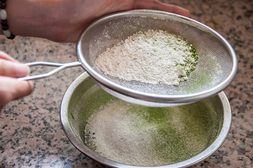A girl sieving flour in bowl in kitchen. The flour is using for making bread.