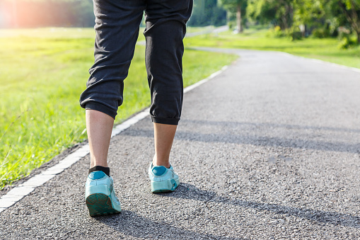 Closeup of female shoe runner feet running on road with nature background, fitness woman
