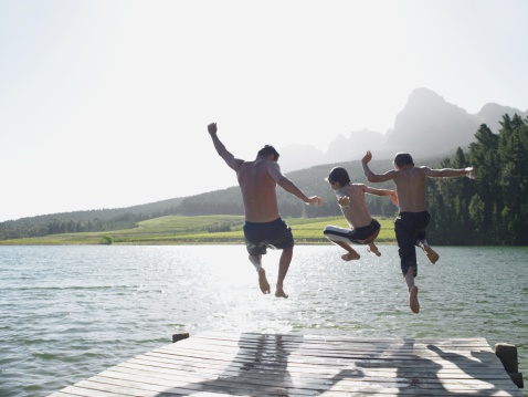 Group of Young Asian man and woman friends with life vest jumping into the lake and swimming together. Happy People enjoy and fun outdoor lifestyle travel nature lake house on summer holiday vacation.