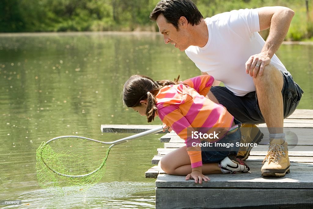 Father and daughter on jetty, holding fishing net - Foto de stock de Pescaria royalty-free