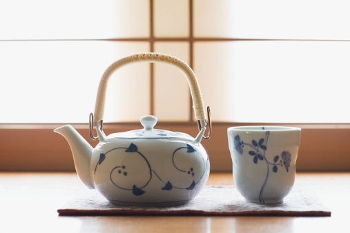Porcelain teapot next to a small heart-shaped bowl with ground tea, a cup with tea and cinnamon sticks.