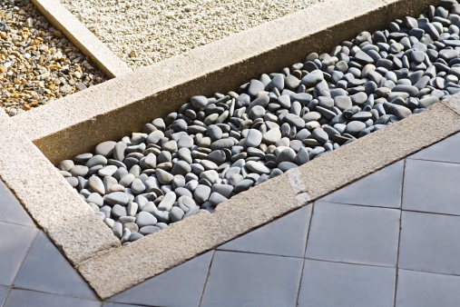 French drain with water Stones near House Wall Windows. Drainage system Stone Water Drains with Storm drain trench grating and Sewage around Building.