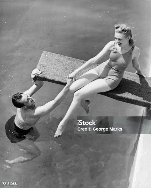 Woman Sitting On Diving Board Man Grasping Her Hand Elevated View Stock Photo - Download Image Now