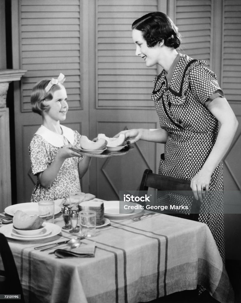 Daughter (8-9) helping mother setting table for breakfast (B&W)  1950-1959 Stock Photo