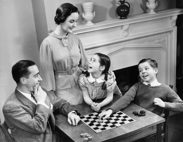 familia con dos hijos (8-9) jugando al ajedrez (b & w). - traditional games fotografías e imágenes de stock