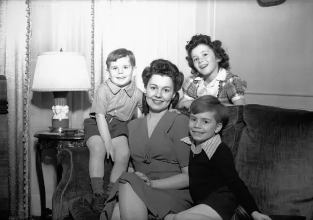 Photo of Mother with three children (4-5, 6-7, 8-9) posing in living room, (B&W), portrait