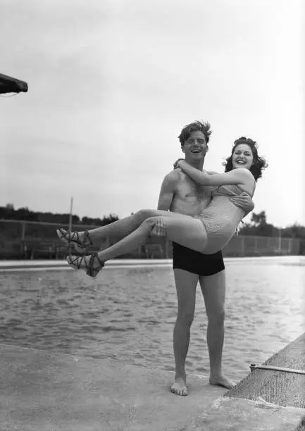 Photo of Man lifting woman at pool edge, (B&W), portrait