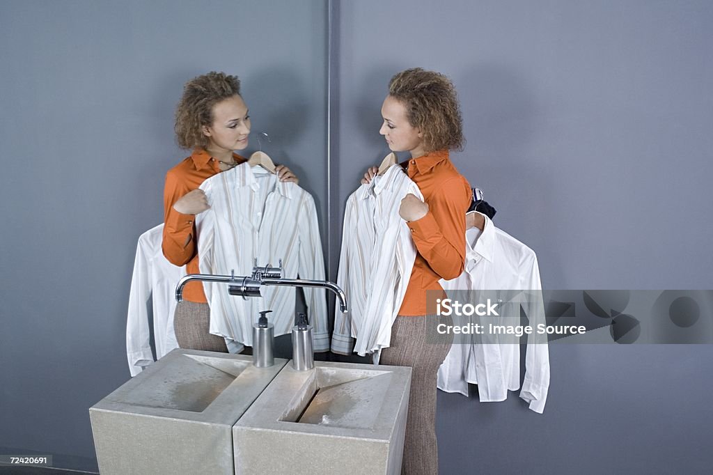 Femme regardant au miroir chemises dans les toilettes - Photo de Femmes libre de droits