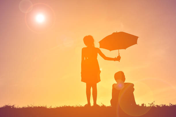 istock Silhouette Sister Holding Umbrella While Brother Sitting On Field Against Sky During Sunset 726846927