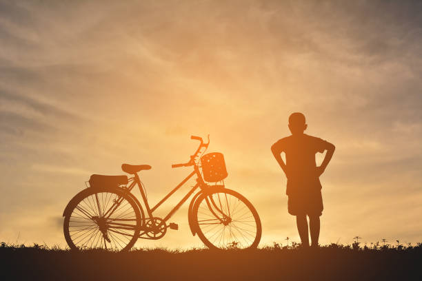 istock Silhouette Boy With Hands On Hip Standing By Bicycle On Field Against Sky During Sunset 727142719