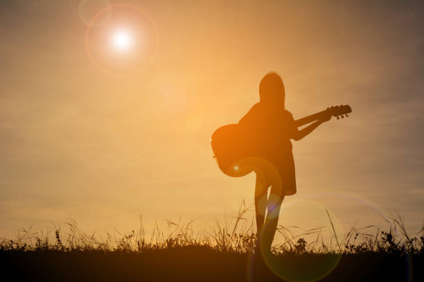 istock Silhouette Girl Playing Guitar While Standing On Field During Sunset 727144167