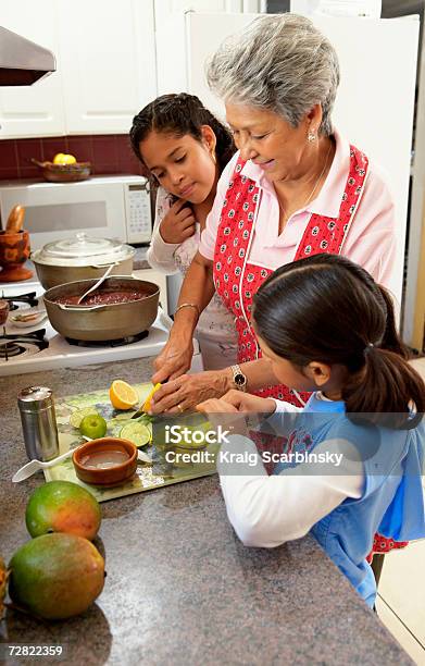 Photo libre de droit de Granddaughters En Regardant La Grandmère À La Cuisine banque d'images et plus d'images libres de droit de Famille