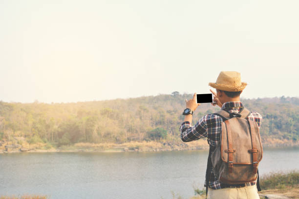 istock Rear View Of Man With Backpack Photographing Lake Using Smart Phone Against Clear Sky 728912089