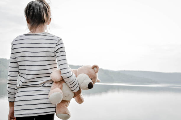 istock Rear View Of Girl Holding Teddy Bear While Standing Against River 730197757
