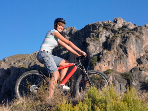 Female mountain biker rides along mountain trail. Front view