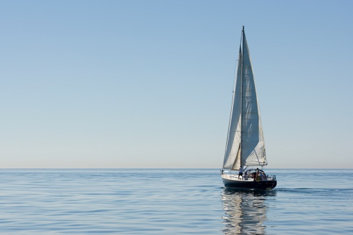 A light blue sailboat is sailing peacefully in Frenchman Bay around the porcupine islands in Bar Harbor Maine.