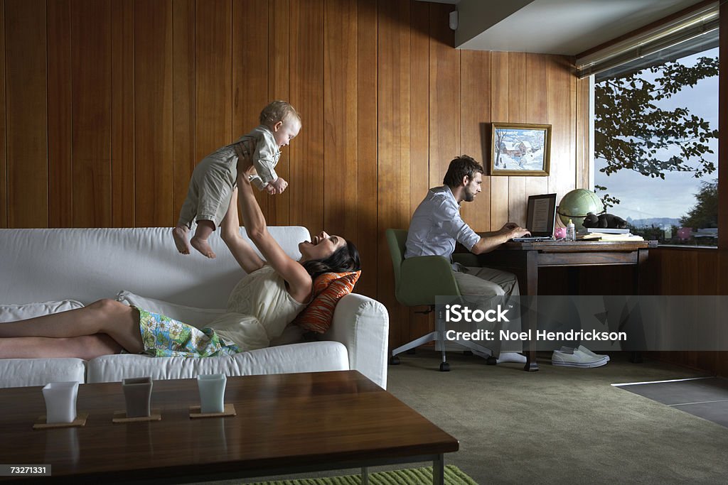 Mother playing with baby girl (6-9 months) while father using laptop in living room  Above Stock Photo