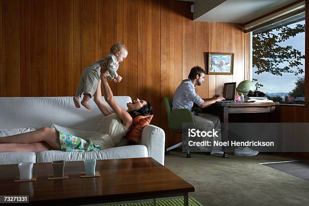 Mother Playing With Baby Girl While Father Using Laptop In Living Room Stock Photo - Download Image Now