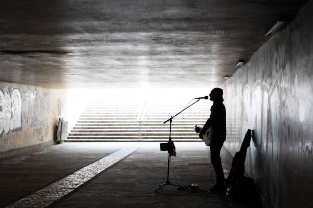 silhouette eines straßenmusikers, der gitarre spielt, während er an einem unterirdischen gehweg singt - street musician stock-fotos und bilder