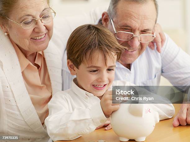 Avós Ensinando Neto Para Poupar Dinheiro Em Um Mealheiro - Fotografias de stock e mais imagens de Riqueza