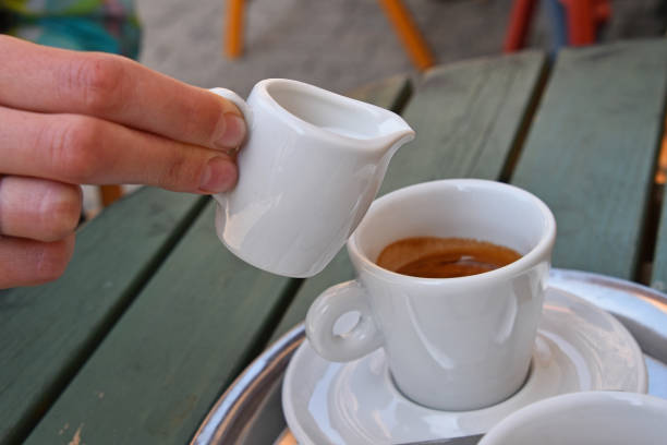 istock Cropped Hand Pouring Milk From Pitcher In Coffee At Table 740623493