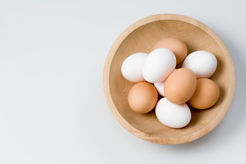Three eggs in a white bowl on a wood table