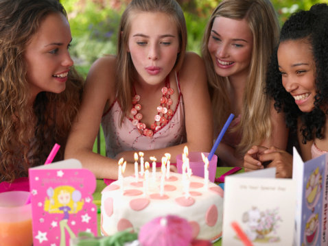 Pretty smiling teenage girls in dresses and crowns holding cake at birthday party od