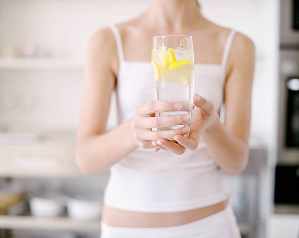 femme tenant le verre d'eau avec citron - water women glass healthy eating photos et images de collection