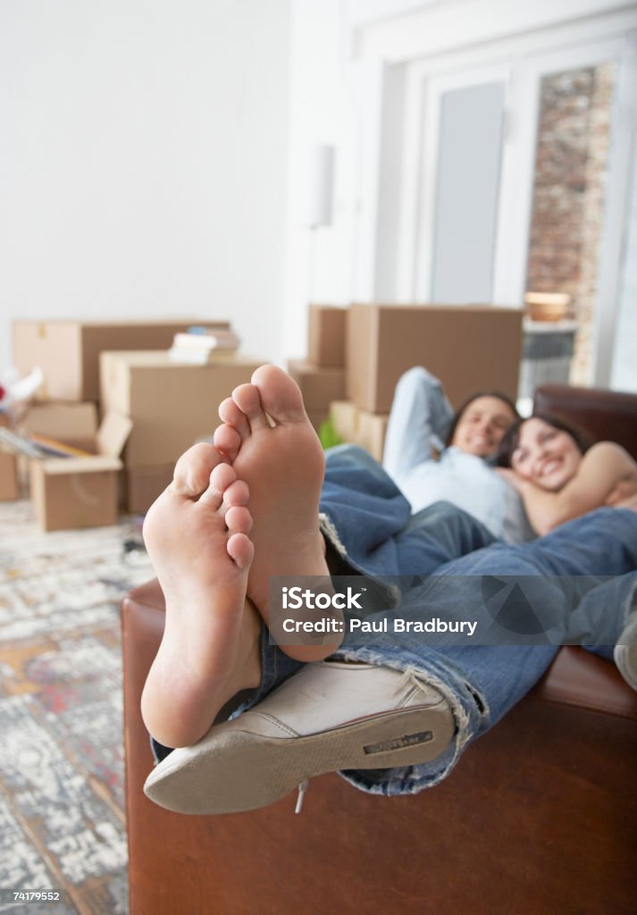 Uomo e donna sdraiato sul divano di casa con cartone - Foto stock royalty-free di Divano