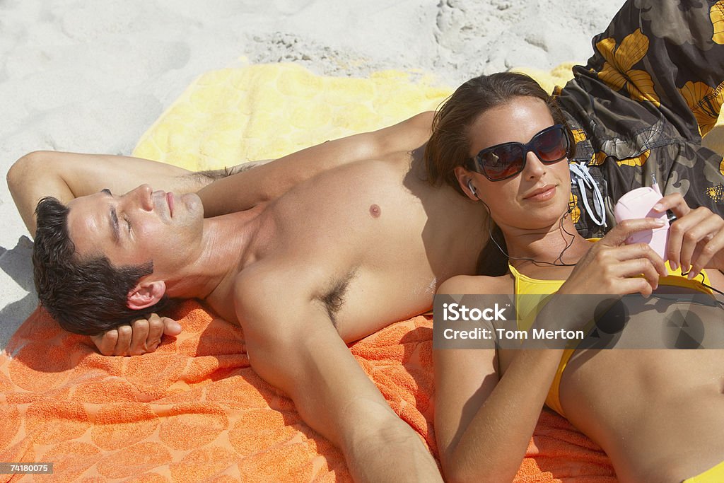 ビキニの女性、MP 3 プレーヤーに横たわる男性 - ビーチタオルのロイヤリティフリーストックフォト