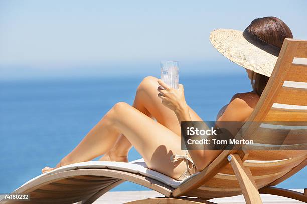Foto de Mulher De Chapéu De Palha Banhos De Sol Em Uma Cadeira De Madeira Com Bebidas e mais fotos de stock de Só Uma Mulher