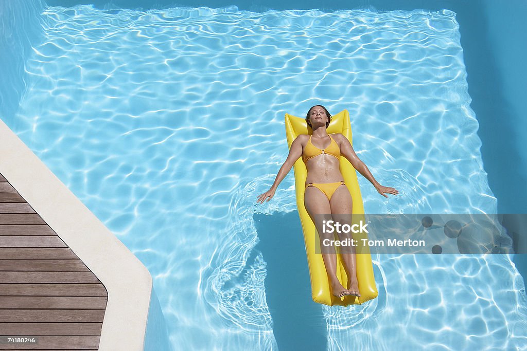 Donna in bikini sul dispositivo di galleggiamento in piscina - Foto stock royalty-free di 20-24 anni