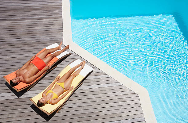 男性と女性のプールデッキでの日光浴 - swimming trunks swimwear summer bikini ストックフォトと画像