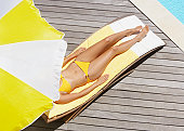Woman sunbathing on pool deck in bikini with umbrella