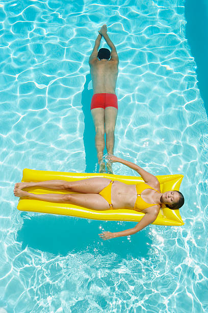mujer en el dispositivo de flotación y hombre de natación en la piscina - swimming trunks bikini swimwear red fotografías e imágenes de stock