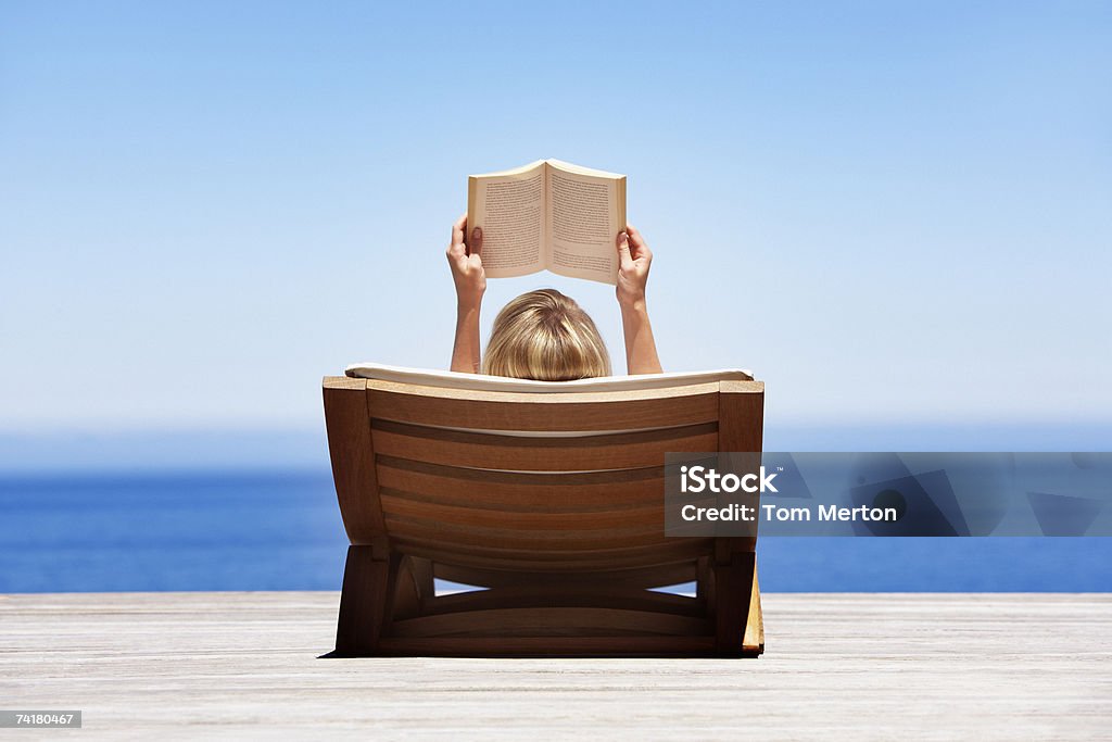 Rear view of woman reading outdoors in wooden chair  Reading Stock Photo