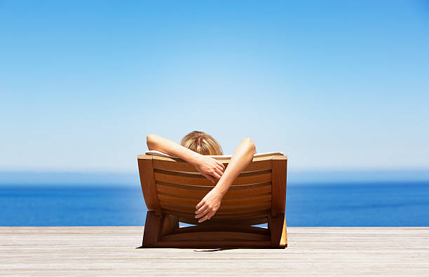 Rear view of woman reclining on folding chair outdoors  deck chair stock pictures, royalty-free photos & images