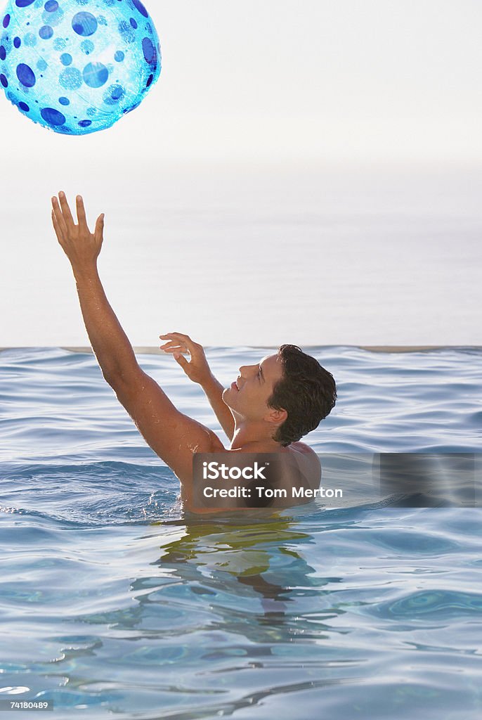 Hombre jugando con una pelota de playa, en la piscina de borde infinito - Foto de stock de 20-24 años libre de derechos