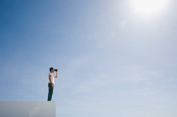 hombre en pedestal con binoculares y azul cielo al aire libre - binaculars fotografías e imágenes de stock