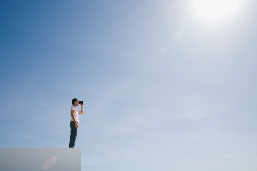 Man on pedestal with binoculars and blue sky outdoors