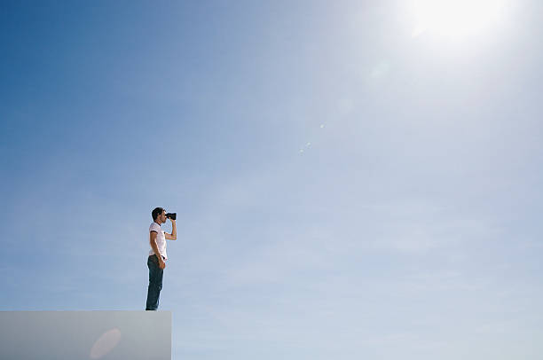 Man on pedestal with binoculars and blue sky outdoors  binoculars photos stock pictures, royalty-free photos & images