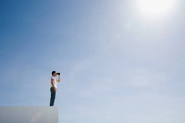 Photo of Man on pedestal with binoculars and blue sky outdoors
