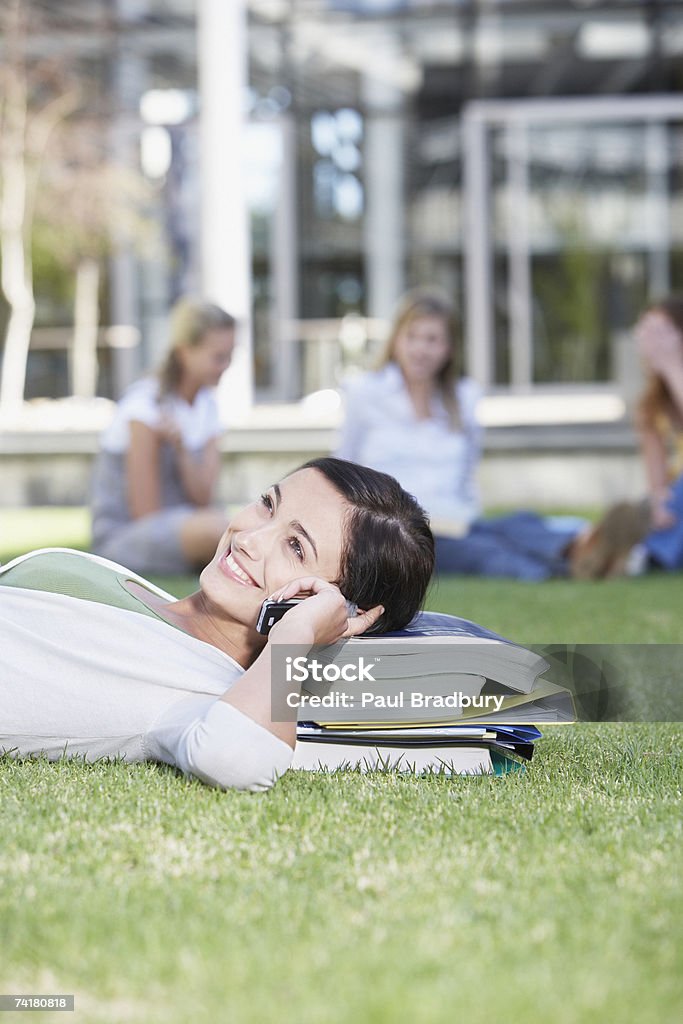 Giovane donna sdraiato nell'erba su libri con cella - Foto stock royalty-free di 18-19 anni