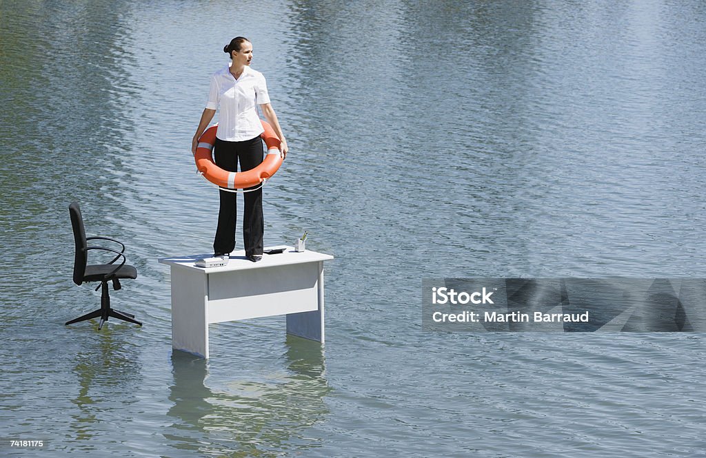 Businesswoman standing on desk with flotation device  Flood Stock Photo