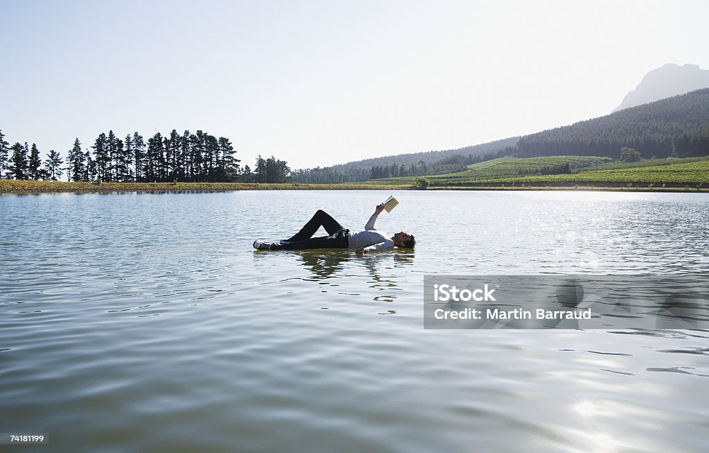 Uomo sdraiato sull'acqua lettura libro - Foto stock royalty-free di 25-29 anni