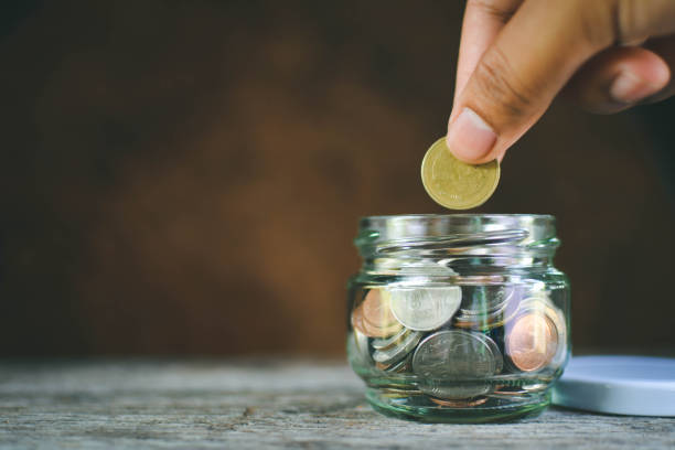 istock Cropped Hand Putting Coin In Glass Container On Wooden Table 746100925