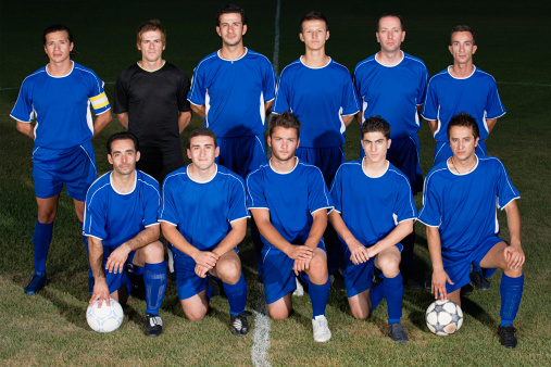 Portrait of female soccer team in white soccer uniforms with senior, gray-haired coach on soccer field