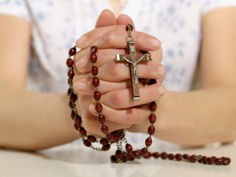 Hands of a young woman praying with rosary